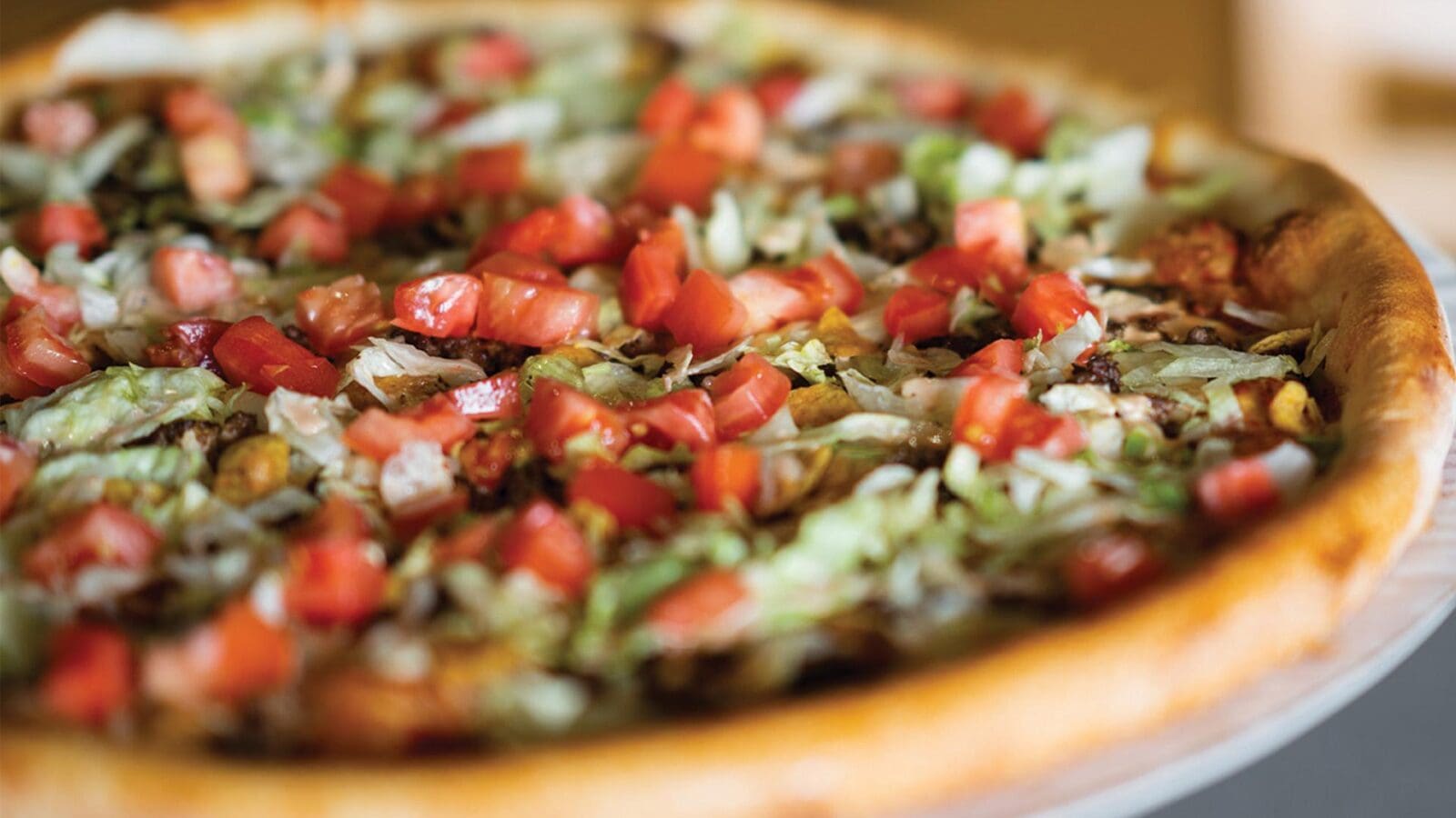 Dewey's Pizza's Tito Santana seasonal pizza topped with melted Chihuahua cheese and cheddar, seasoned ground beef, red onions, fresh shredded lettuce, diced tomatoes, crumbled corn chips, and a drizzle of chipotle ranch.