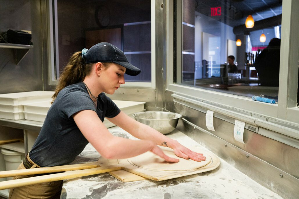 a dewey's employee stretches a pizza dough