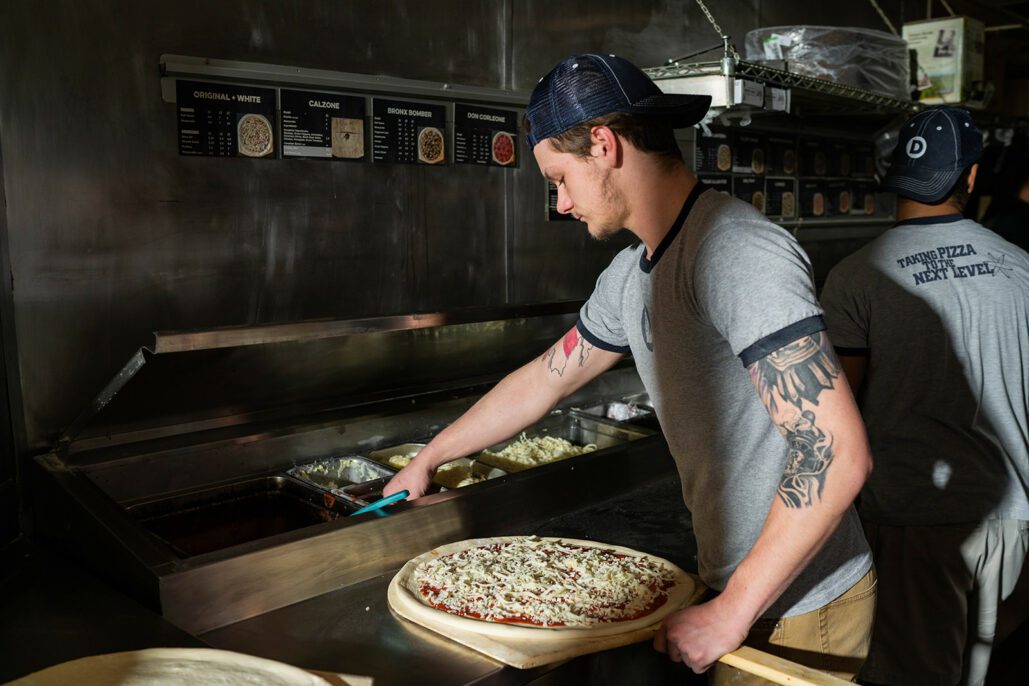 a dewey's employee adds toppings to a pizza