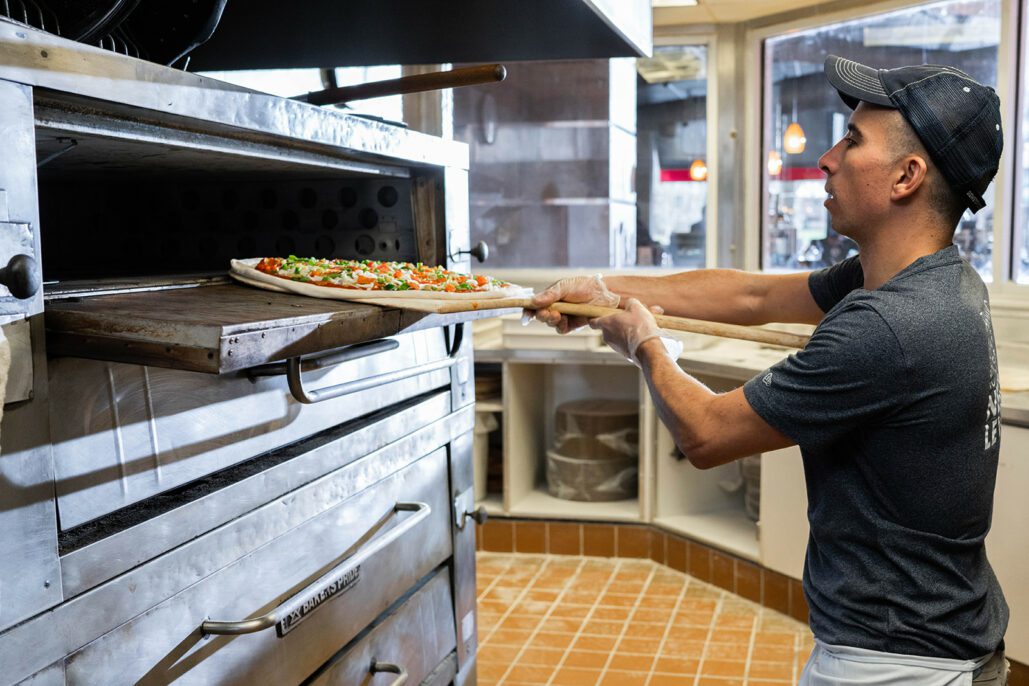a dewey's employee places a pizza into the oven