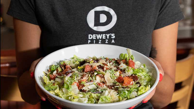 a person wearing a dewey's tshirt holds up a salad