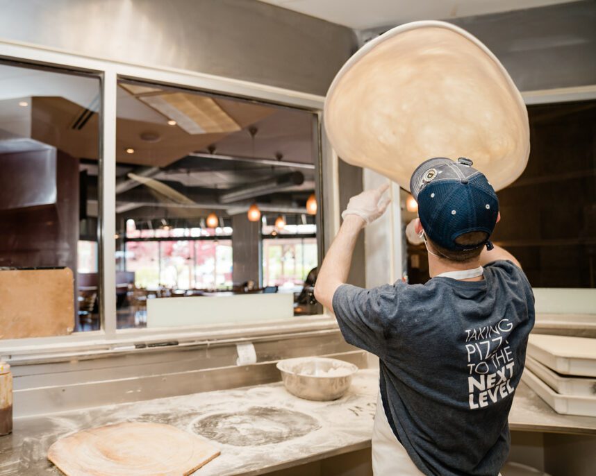 a dewey's employee tosses a pizza crust into the air