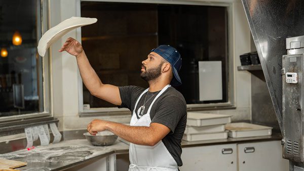 A Dewey's Pizza employee tosses pizza dough into the air