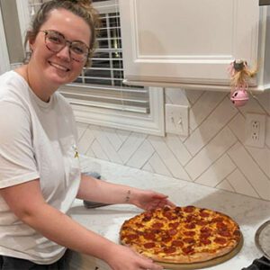 a woman proudly showing off her baked pepperoni pizza