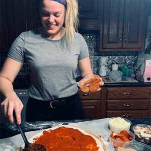a woman adding sauce to a pizza dough