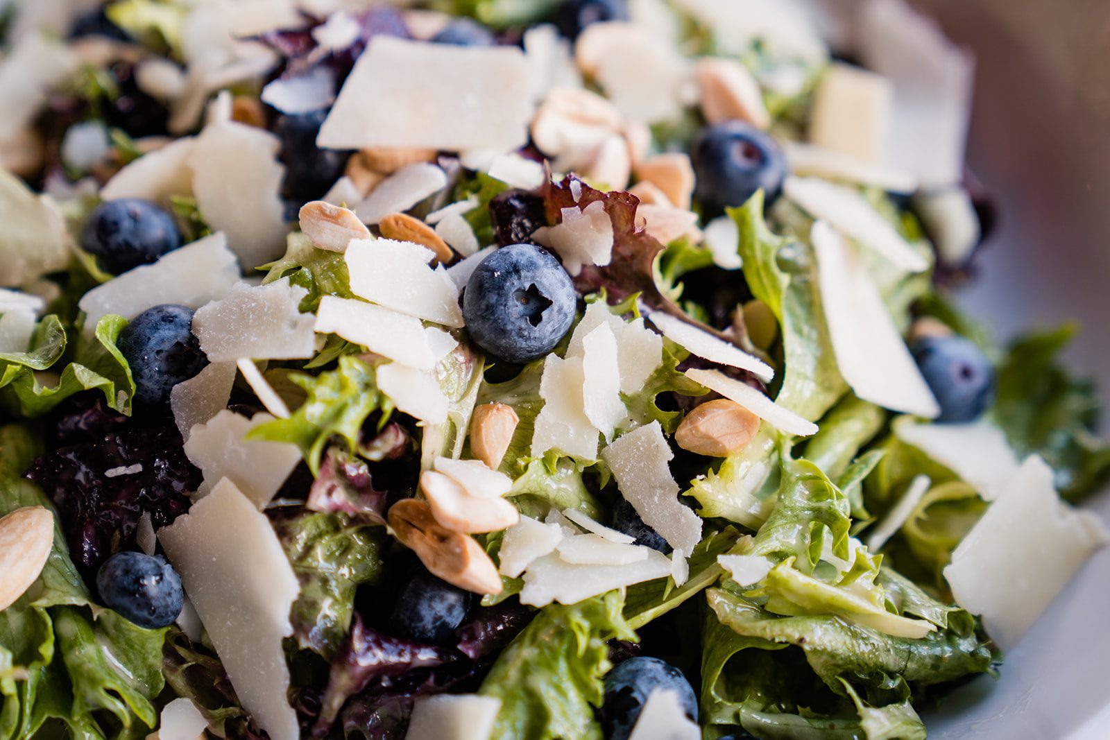 Close-up of Dewey’s seasonal salad, Blueberry Almond, featuring Field Greens, Fresh Blueberries, Marcona Almonds, Parmesan Cheese, and Housemade Lemon-Ginger Vinaigrette Dressing
