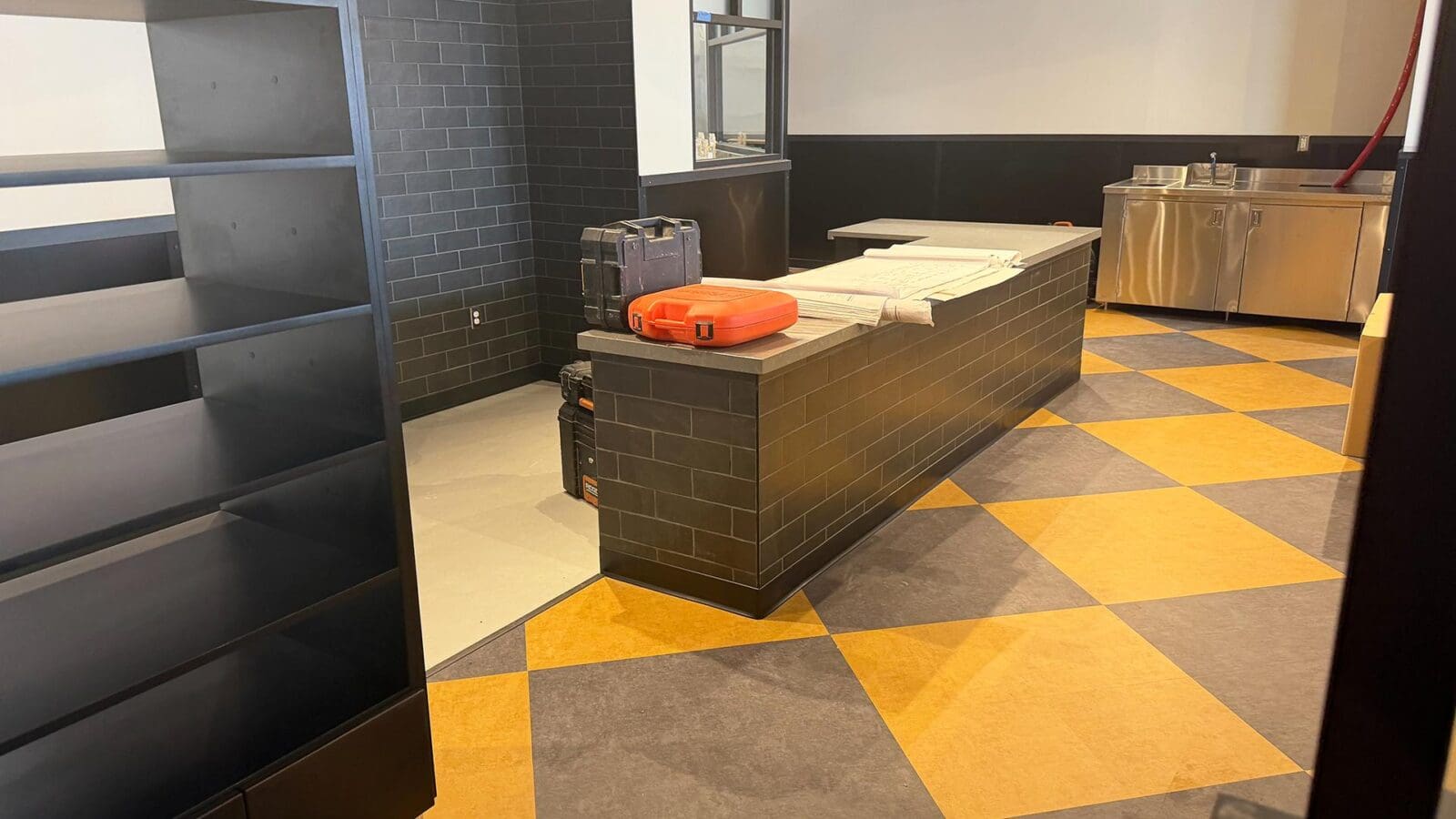 Construction progress at the new Dewey's Pizza in Creve Coeur, featuring blueprints and tools on a newly tiled service counter with a yellow and dark gray checkered floor.