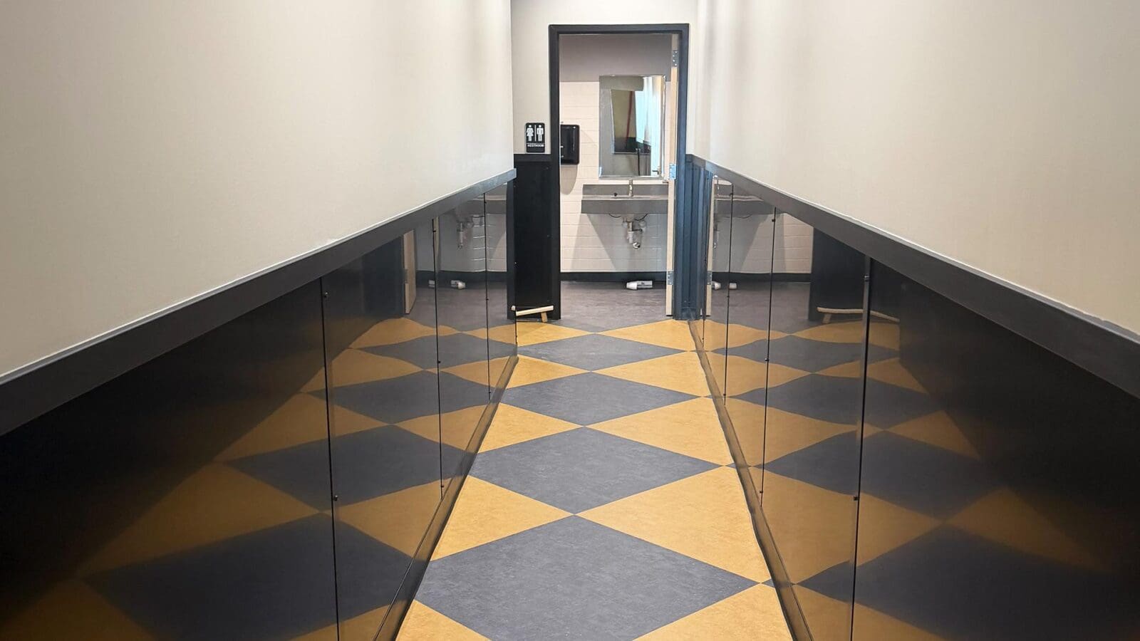 A brightly lit hallway inside the new Dewey's Pizza in Creve Coeur, featuring a yellow and dark gray diamond-patterned floor leading to an open restroom door.