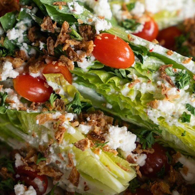 Close-up of Dewey’s Pizza Sweet Vidalia Wedge salad. Featuring ingredients including Baby Romaine, Sweet Onion Dressing, Feta, Grape Tomatoes, Fried Onions, Parsley.
