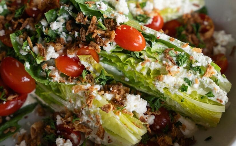 Close-up of Dewey’s Pizza Sweet Vidalia Wedge salad. Featuring ingredients including Baby Romaine, Sweet Onion Dressing, Feta, Grape Tomatoes, Fried Onions, Parsley.